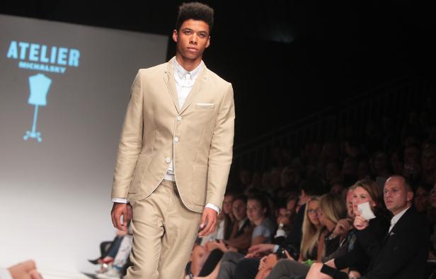Ein Mann präsentiert ein beigefarbenes Jackett und eine Hose auf dem Laufsteg.