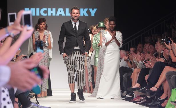 Ein Designer läuft über den Laufsteg, gefolgt von Models bei einer Modenschau.