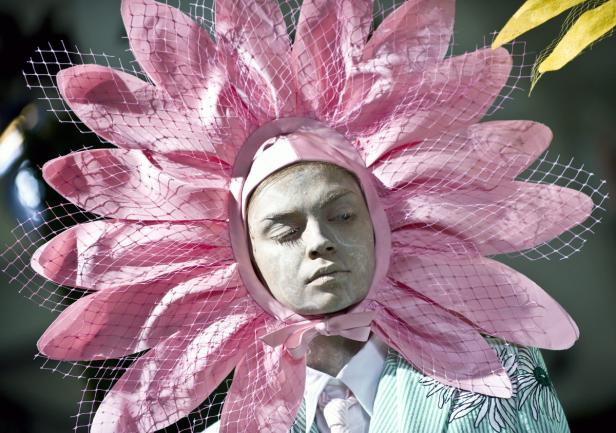 Eine Person mit weißer Schminke trägt ein rosa Blumenkostüm.