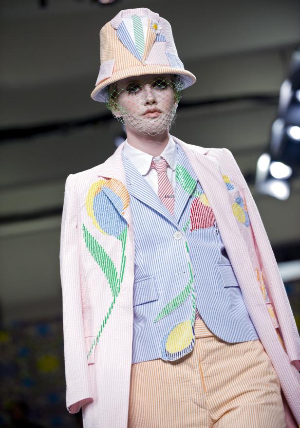 Ein Model mit Hut und Schleier präsentiert ein gestreiftes Hosenanzug mit Blumenapplikationen.