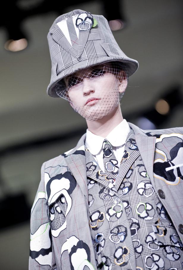 Ein Model trägt einen karierten Huthut mit Schleier und einen passenden Anzug mit Blumenmuster.