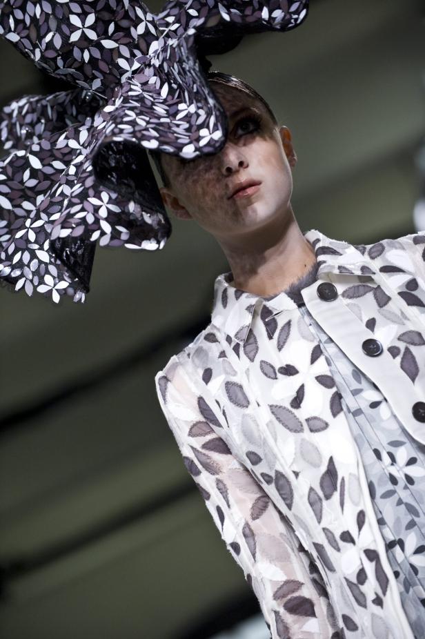 Ein Model mit einem extravaganten Hut und einem passenden Blazer mit Blumenmuster präsentiert ein Mode-Design.