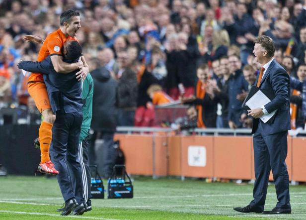 Ein Fußballspieler wird von einem Teamkollegen umarmt, während der Trainer lächelt.