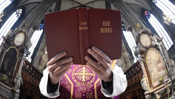 Ein Priester hält in einer Kirche eine aufgeschlagene Bibel in den Händen.