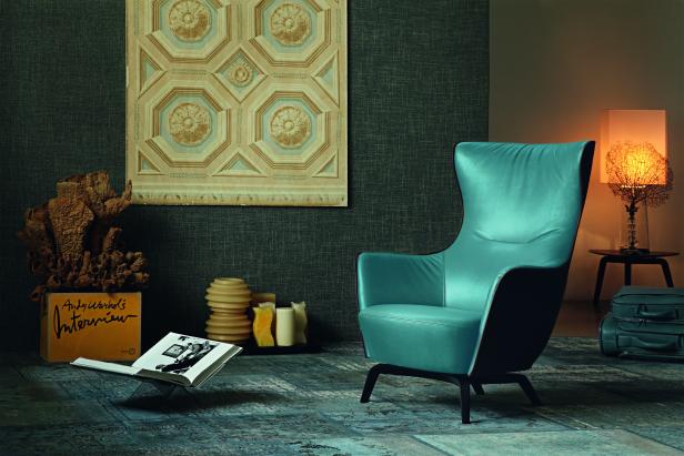 Ein türkisfarbener Sessel steht in einem eleganten Wohnzimmer mit Kunst und Designelementen.
