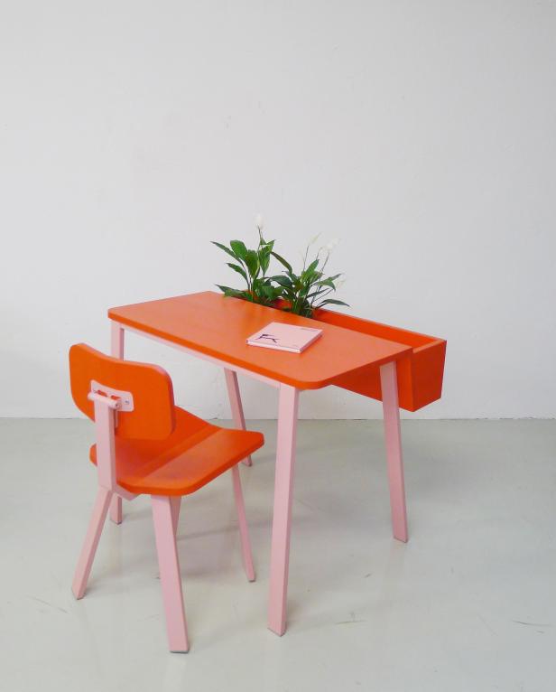 Ein orangefarbener Kinderschreibtisch mit rosa Beinen und einem Stuhl vor einer weißen Wand.