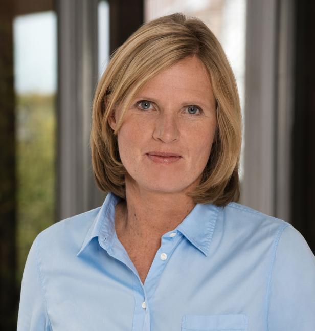 Eine Frau mit blonden Haaren und einem hellblauen Hemd blickt in die Kamera.