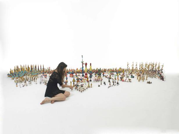 Eine Frau in einem schwarzen Kleid arrangiert eine Sammlung von Holzfiguren auf einem weißen Hintergrund.