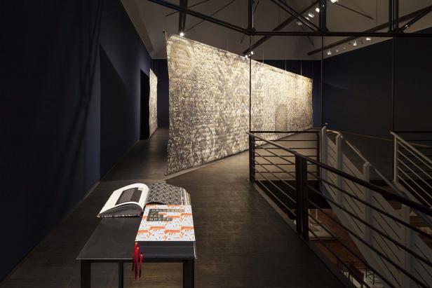 In einem Ausstellungsraum hängen große Stoffbahnen mit Schriftzeichen und Mustern.