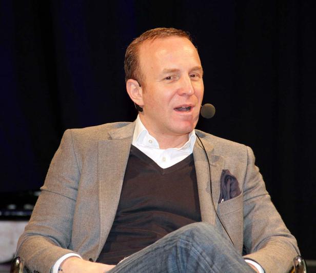 Ein Mann mit Mikrofon spricht vor einem dunklen Hintergrund.