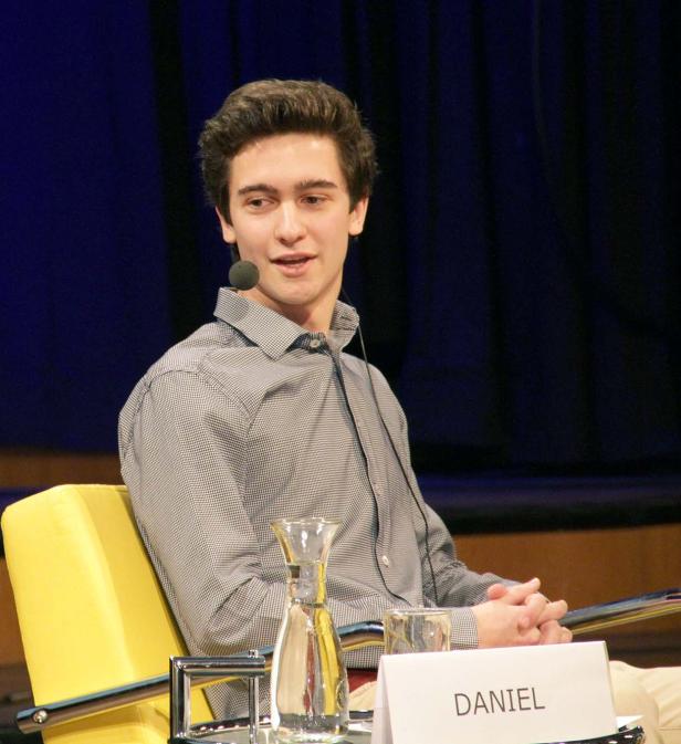 Ein junger Mann namens Daniel sitzt bei einer Veranstaltung auf einem gelben Stuhl.