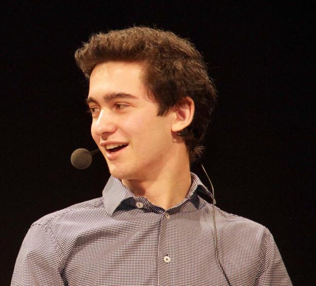 Ein junger Mann mit Mikrofon lächelt und schaut zur Seite.