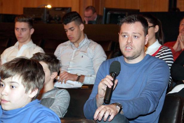 Ein Mann spricht in ein Mikrofon vor einem Publikum.