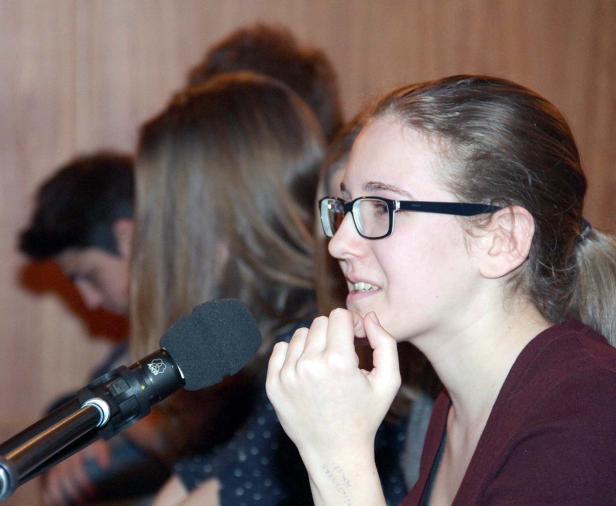 Eine junge Frau mit Brille spricht in ein Mikrofon.