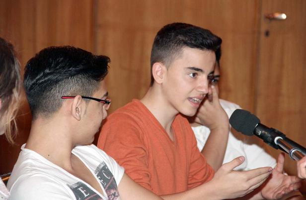 Ein junger Mann spricht in ein Mikrofon, während andere ihm zuhören.