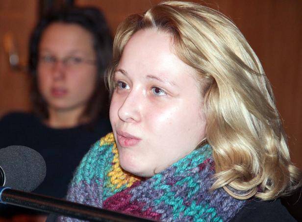 Eine Frau mit blonden Haaren und einem bunten Schal spricht in ein Mikrofon.