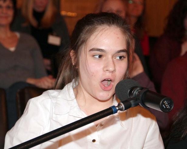 Ein junges Mädchen spricht in ein Mikrofon vor einem Publikum.