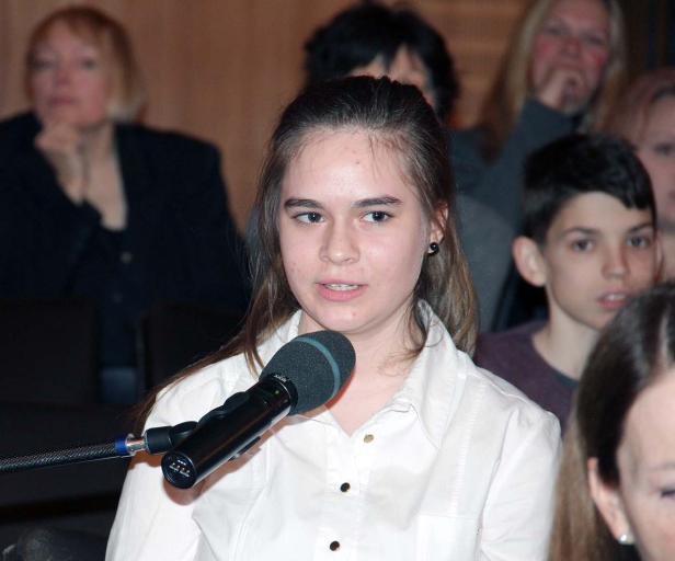 Ein junges Mädchen spricht in ein Mikrofon vor einem Publikum.