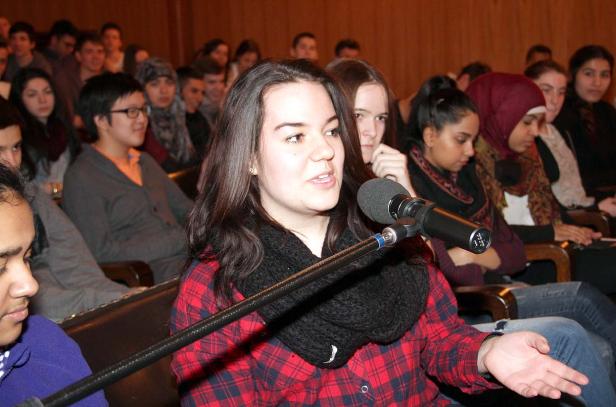 Eine junge Frau spricht vor einem Publikum in ein Mikrofon.