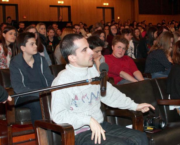 Ein Mann spricht vor einem Publikum in einem Auditorium, eine Kamera liegt neben ihm.