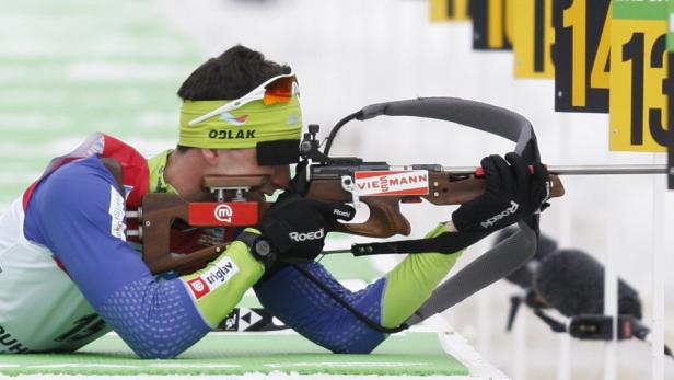 Ein Biathlet zielt liegend mit einem Gewehr auf eine Zielscheibe.