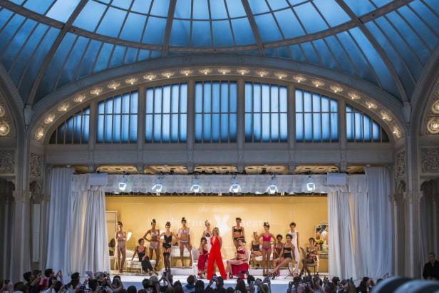 Eine Modenschau mit Models in Dessous auf einer Bühne vor einem großen Publikum.