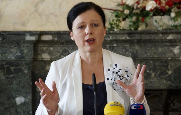 Eine Frau in einem weißen Blazer spricht vor Mikrofonen.