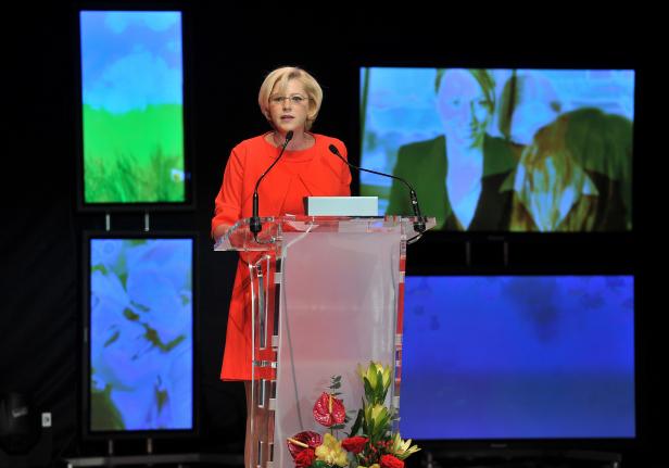 Eine Frau in einem roten Kleid spricht auf einer Bühne hinter einem Rednerpult.