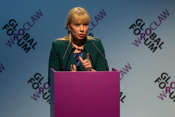 Eine Frau mit blonden Haaren spricht an einem violetten Rednerpult.