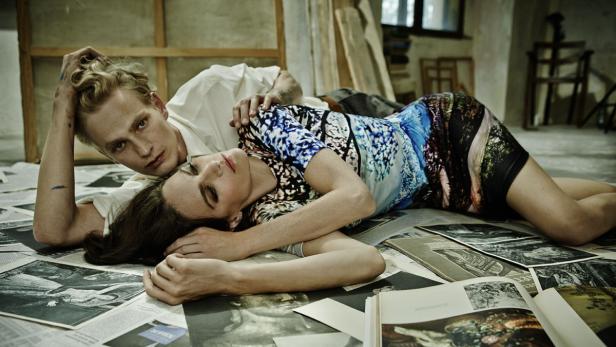 Ein Mann und eine Frau liegen auf dem Boden, umgeben von Zeitungen und Kunstbüchern.
