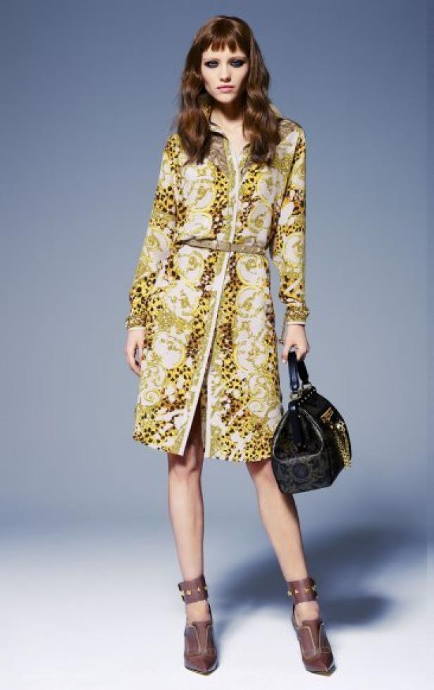 Eine Frau in einem gemusterten Hemdkleid mit Gürtel und braunen Schuhen hält eine Handtasche.