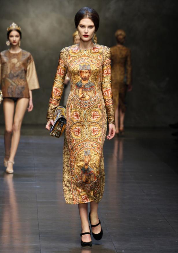 Eine Frau auf dem Laufsteg, die ein langes Kleid mit einem Mosaikmuster und Abbildungen von Königen trägt.