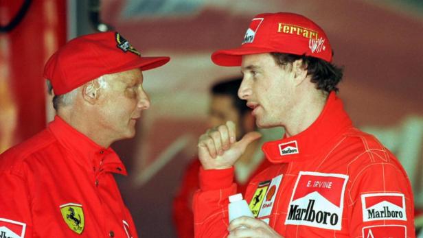 Niki Lauda und Eddie Irvine im Gespräch, beide in roter Ferrari-Rennbekleidung.