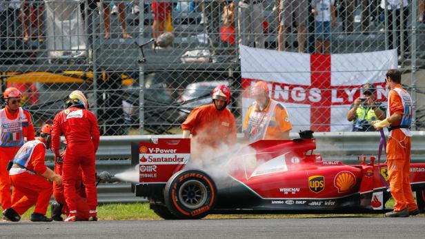 Rennstreckenpersonal löscht einen brennenden Ferrari-Rennwagen.