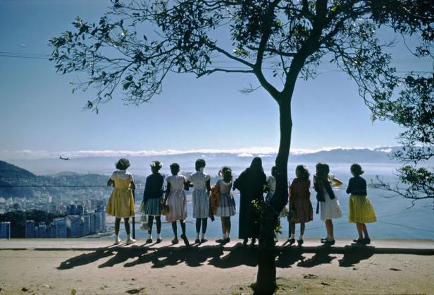 Eine Gruppe von Mädchen und eine Nonne blicken auf eine Stadt am Meer.