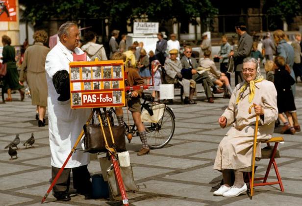 Ein Passfotograf macht ein Foto von einer älteren Dame auf einem belebten Platz.