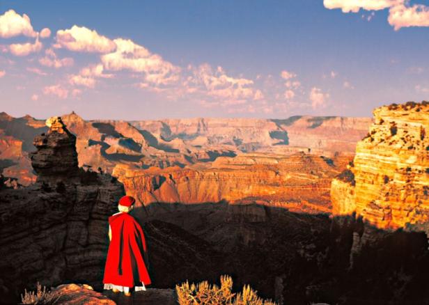 Eine Person in rotem Umhang steht am Rande des Grand Canyon.