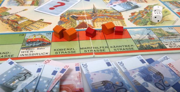 Ein Spielbrett mit Holzhäusern, Würfeln, Spielkarten und Euro-Banknoten.