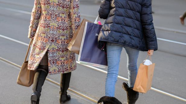 Zwei Frauen mit Einkaufstüten überqueren eine Straße mit Straßenbahnschienen.