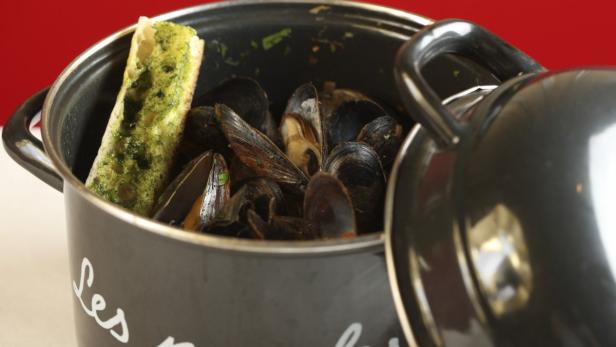 Ein Topf mit Miesmuscheln und einem Stück Brot mit Kräuterbutter.