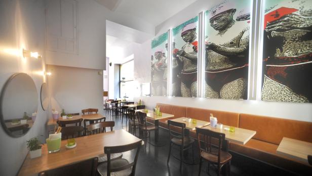 Innenansicht eines Restaurants mit Holztischen, Stühlen und einem Wandbild.