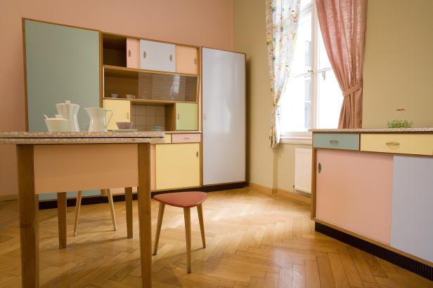 Eine Küche im Retro-Stil mit bunten Schränken, einem Tisch und einem Hocker.