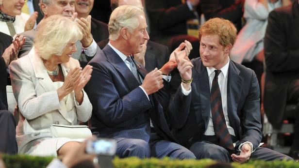 König Charles, Prinz Harry und Königin Camilla bei einer Veranstaltung, bei der sie applaudieren.