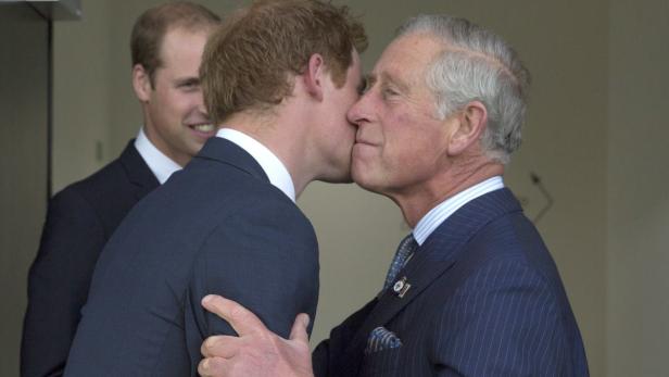 Prinz Harry küsst König Charles, während Prinz William im Hintergrund lächelt.