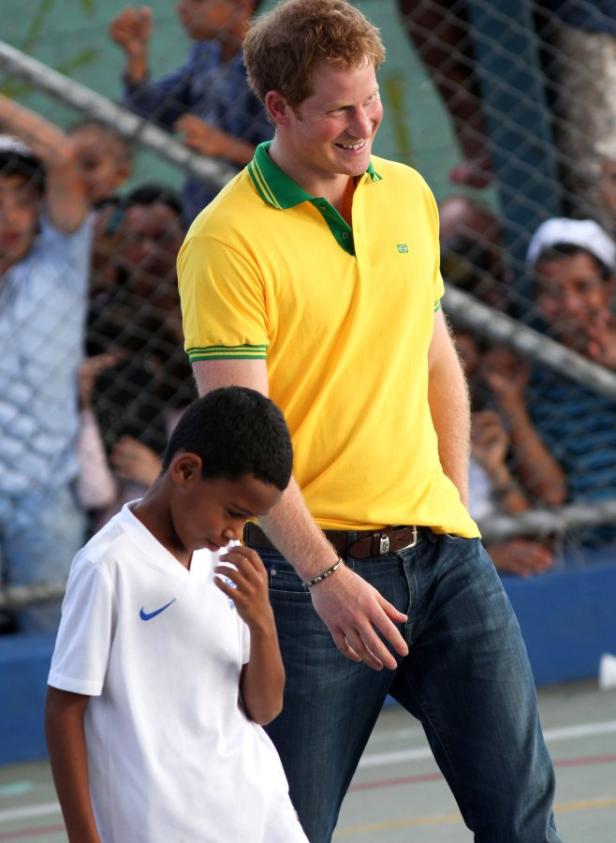Prinz Harry in einem gelben Poloshirt mit einem Jungen in einem weißen Fußballtrikot.