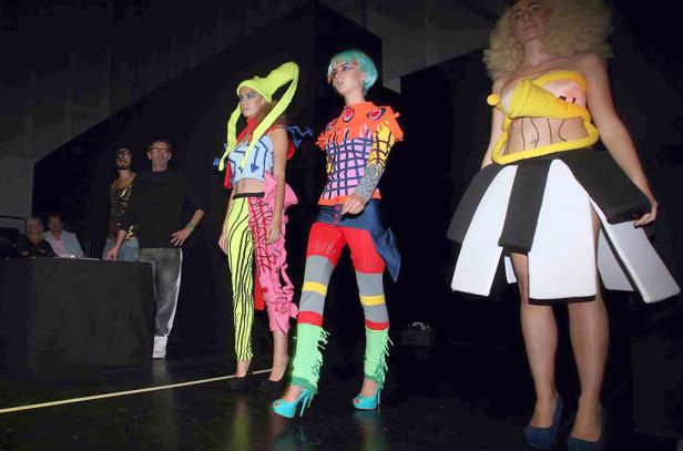 Drei Models präsentieren extravagante Mode auf einem Laufsteg.