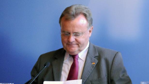 Ein Mann mit Brille und Anzug steht vor einem Mikrofon und liest ein Dokument.