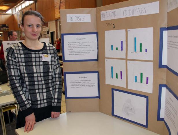 Eine junge Frau steht vor einer Präsentation über Hunde auf einer Wissenschaftsmesse.