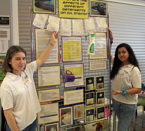 Zwei Schülerinnen präsentieren ein Projekt über die Wirkung verschiedener Reinigungsmittel auf Ölflecken.