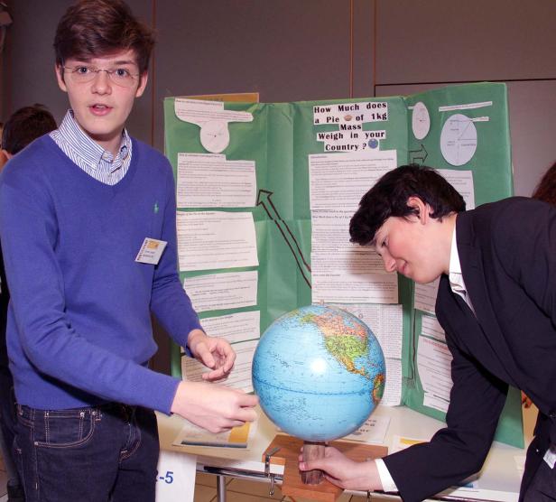Zwei Jugendliche präsentieren ein Projekt über das Gewicht eines Kilos auf der Erde anhand eines Globus.